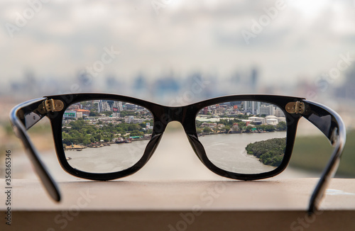 Black eyeglass on a reflective surface. View through the lens of glasses that look at the Chao Phraya River.