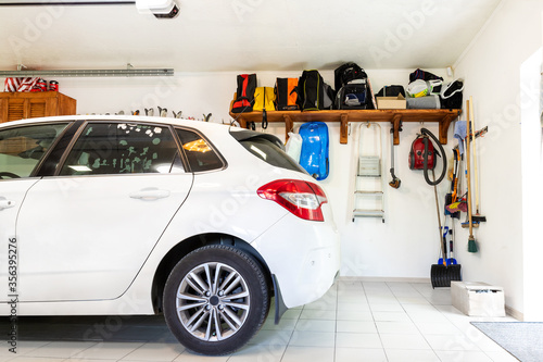 Home suburban car garage interior with wooden shelf , tools and equipment stuff storage warehouse on white wall indoors. Vehicle parked at house parking background