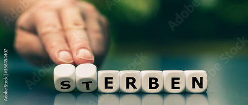 Hand dreht Würfel und ändert das Wort "Sterben" in "Erben".