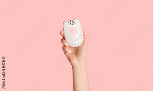 Unrecognizable millennial girl showing modern electric epilator on pink background