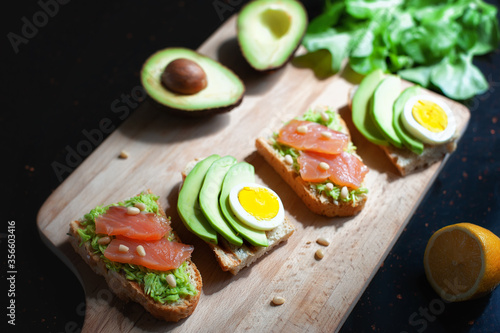 lemon and sandwiches with avocado, sliced egg, red fish and pine nuts on a wooden cutting board on the dark stone countertop