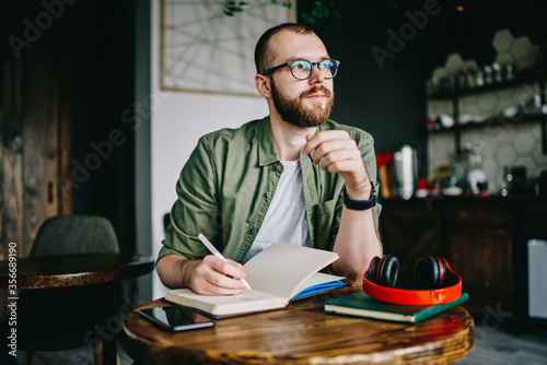 Handsome creative author sitting at cafe interior with notebook