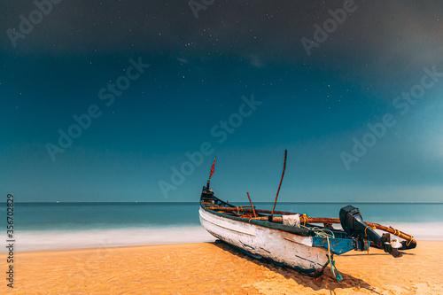 Goa, India. Real Night Sky Stars. Natural Starry Sky Blue Color Above Sea Seascape Ocean Beach. Background. Parked Old Wooden Boat At Coast