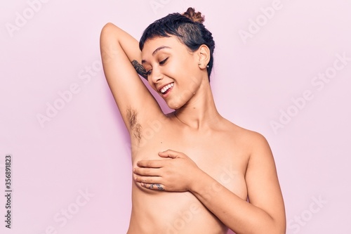 Young beautiful woman shirtless smiling happy. Standing with smile on face showing hairy armpit over isolated pink background