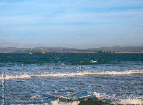 An oil tanker and a sailboat sail along the Cantabrian Sea near the bay of Santander