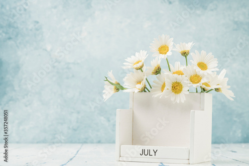 White cube calendar for july decorated with daisy flowers on table with copy space