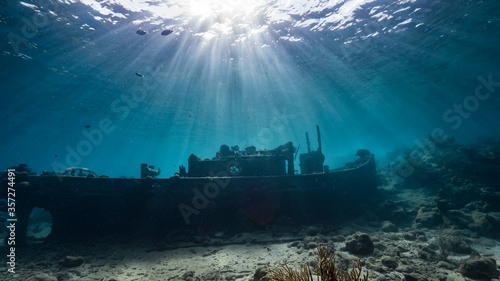 Ship wreck "Tugboat" in shallow water of coral reef in Caribbean sea / Curacao with view to surface and sunbeam