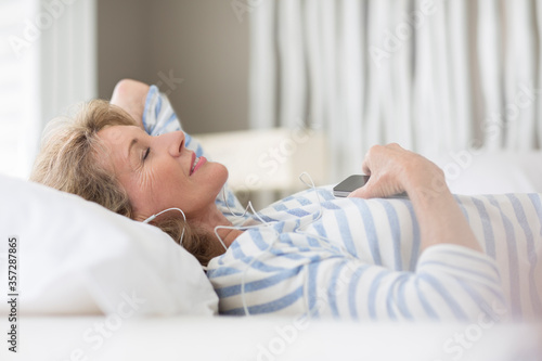 Older woman listening to earphones on bed