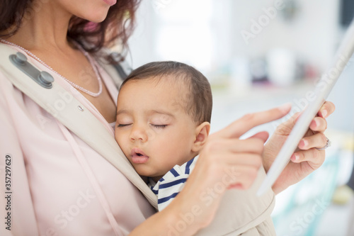 Mother with sleeping baby girl using digital tablet