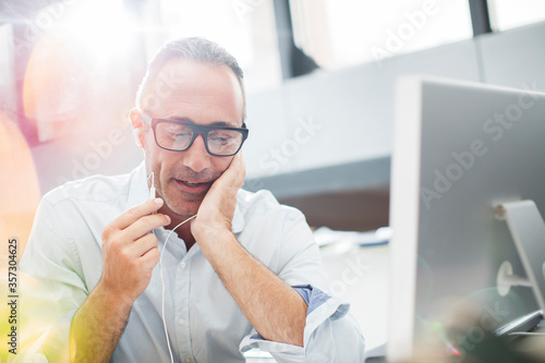 Businessman listening to earbuds at office desk