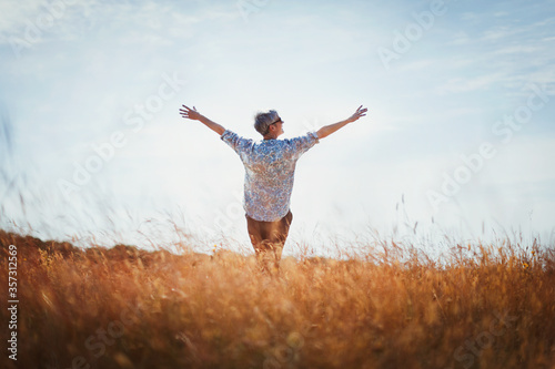 Exuberant senior woman with arms outstretched in sunny field