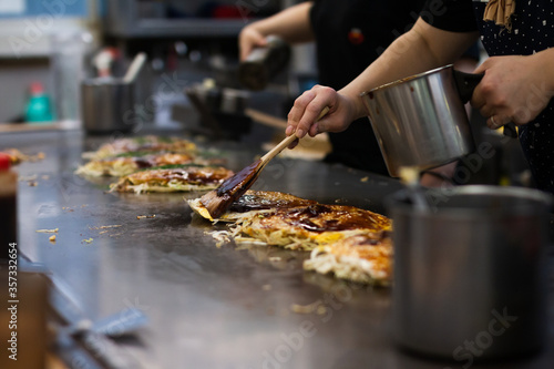 Making a Hiroshima style layered pancake, Okonomiyaki on a hot pan.