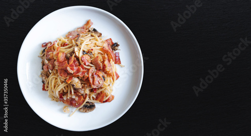 Stir fry Spaghetti bacon with Champion mushroom in white dish on black stone table top, with copy space