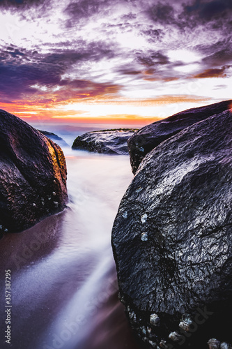 Beautiful sunrise over the beach in long exposure. Moving elements sunrise and wave photography from the rocky beach in india. Red sky in bay of bengal , slow-shutter Sea Waves and Rocks photography.