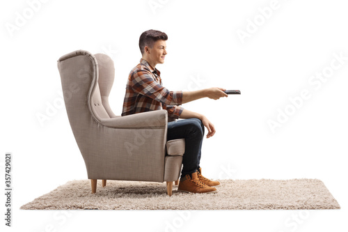 Profile shot of a guy sitting in an armchair and holding a tv remote control