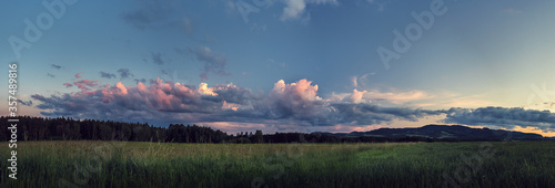 panorama landscape at sunset - meadow, forest and hills and clouds illuminated by the setting sun