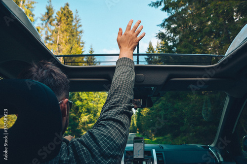 man catch wind with hand through opened sunroof while driving a car