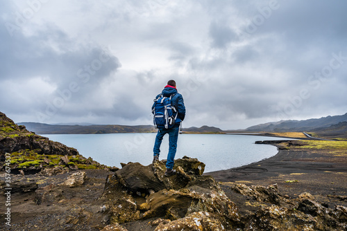 Man hiking in Iceland standing on the peak of rocks with backpack looking at the stunning view near the Kleifarvatn lake in Reykjanesfólkvangur nature reserve park