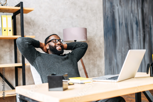 Take a break on a workplace. A young African-American guy leaned back in his chair relaxed, he is pleased with the work done