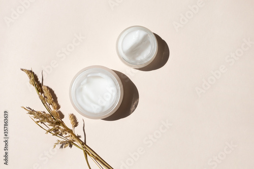 Moisturizer creams and dry meadow herbs on beige background, top view. Care for sensitive skin with natural extract. Summer or autumn skincare body care concept