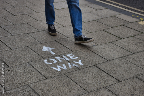 Oxford, UK- 06 13 2020: Oxford introduces social distancing to the city centre streets. Here a person walks past a pavement sign in the wrong direction