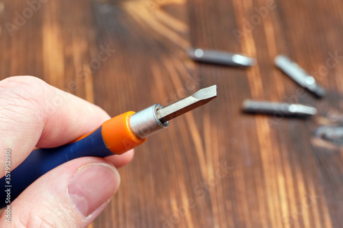 Hand holds screwdriver with interchangeable nozzle with spatula on wooden background.