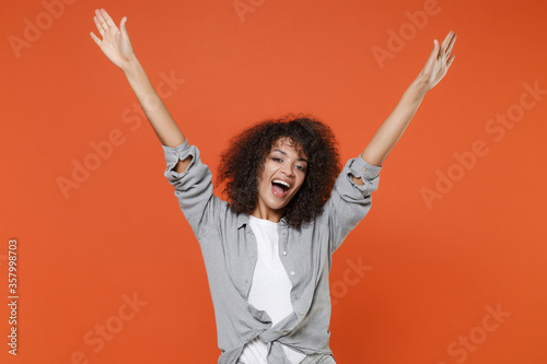Excited joyful young african american woman girl in gray casual clothes isolated on orange background studio portrait. People emotions lifestyle concept. Mock up copy space. Rising spreading hands.