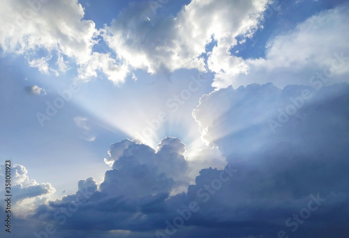 The sun's rays behind the cumulus clouds in blue sky