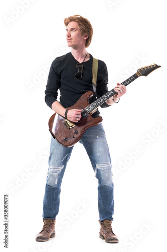 Cool handsome confident young rock music guitarist playing electric guitar looking up. Full body length isolated on white background. 