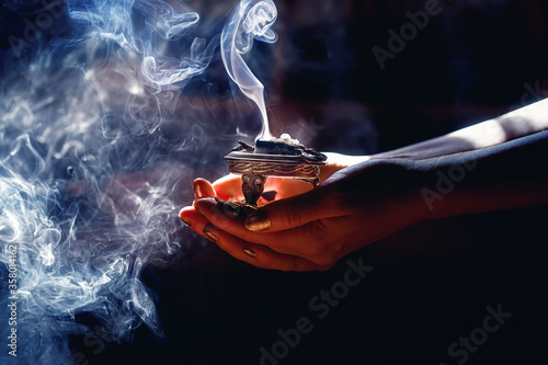 incense in a woman hand, incense smoke on a black background.