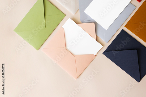 Close-up colorful mail envelopes on beige background flat lay with copy space, top view. Mailing concept isometric. White paper blank mockup for letters, greeting card, postcard, invitation