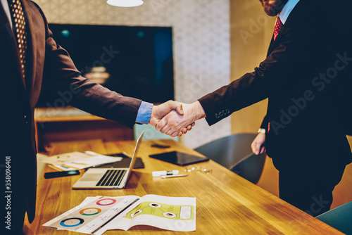 Cropped image of men in suits shaking hands making deal of sponsorship in business corporation, male entrepreneurs agree in partnership cooperation and contract during formal meeting in office