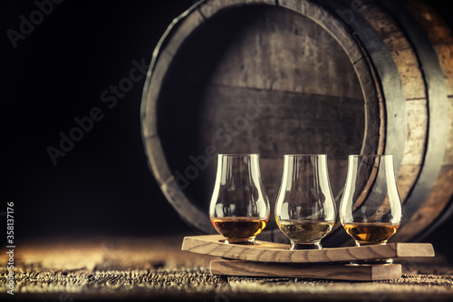 Glencairn whiskey tasting cups on a wooden serving, with a whisky barrel in the dark background