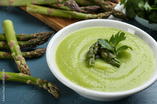 Delicious asparagus soup served on blue wooden table, closeup