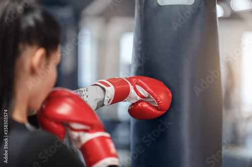 Female boxer in gloves hitting big punching ball during self defence class at gym, empty space