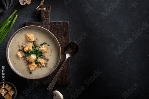 mushroom cream soup with champignons and croutons in a ceramic bowl on a black background, top view, place for text