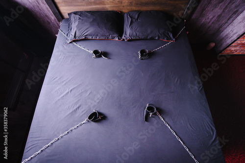 Bedroom for intimate meetings. VDSM equipment and sex toys. Leather handcuffs with a chain on a gray sheet. Fifty shades of gray. Fetish domination.