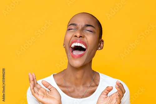Close up portrait of happy young African American woman laughing out loud with both hands in clapping gesture isolated studio yellow background