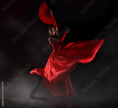 Flamenco woman spanish dancer in red dres performs with fan in dance at black background, studio shot