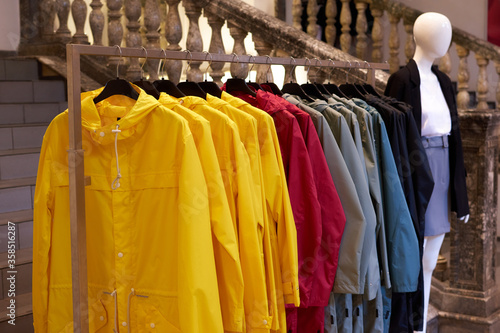 Bright colorful autumn raincoats hanging at a fashion store. Closeup of multi-colored yellow, red, grey, blue waterproof raincoats hang in a row on a hanger at clothes shop in the shopping mall.