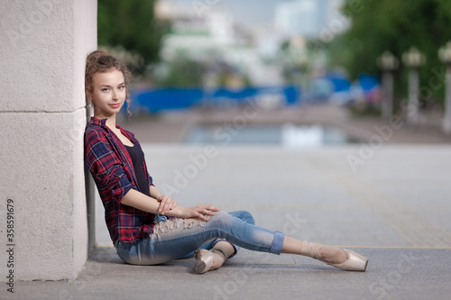 Girl ballerina in jeans, a plaid shirt and pointe shoes dancing in the city on the street