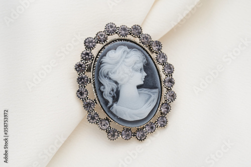 Cameo brooch, which is a side portrait of a woman, with small crystals around the edges on a white background.