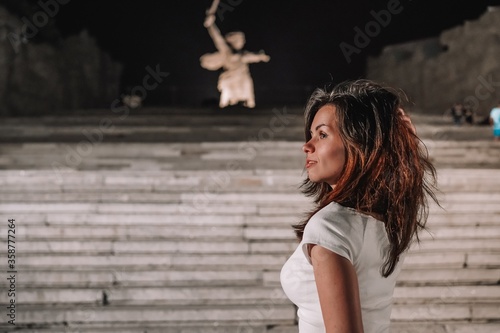 Portrait of a brunette girl with long hair at night against the background of Mamayev Kurgan and sculpture