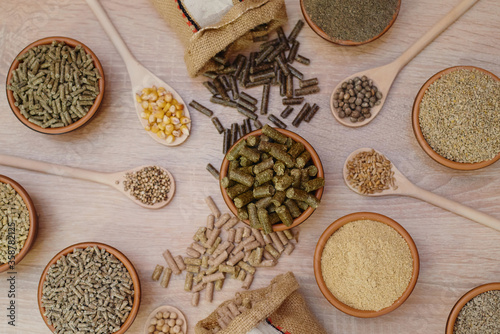 Different kinds of pelleted compound feed in bowls and spoons on wood table, copy space. Top view, flat lay