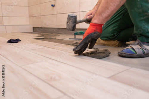 A worker laying ceramic tiles in the bathroom with a rubber mallet gently aligns the floor plane.
