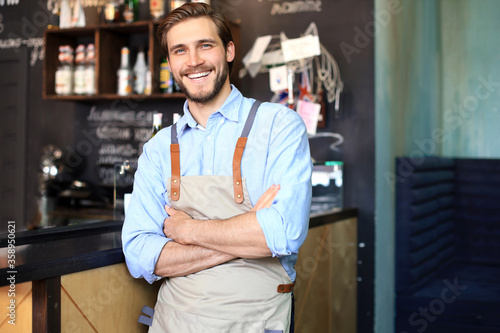 Male business owner behind the counter of a coffee shop with crossed arms, looking at camera.