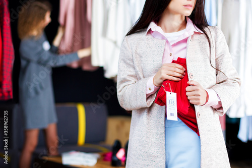 Closeup of young woman is stealing red jeans in store, shop, boutique at shopping center. Girl is hiding unpaid good under clothes. Seller, assistant caught thief on hot. Shoplifting concept.