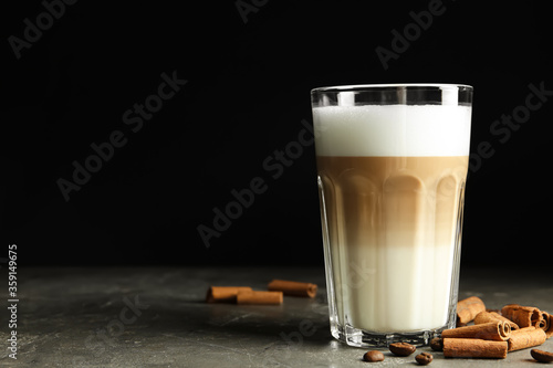 Delicious latte macchiato and cinnamon on grey table against black background, space for text