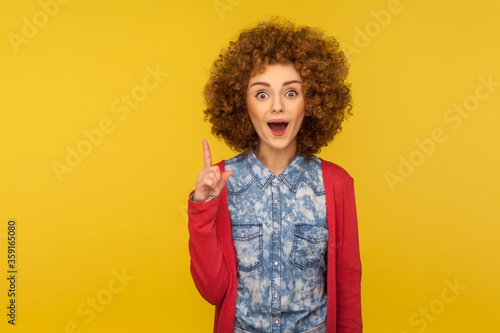 Eureka, I know answer! Portrait of amazed inspired woman with curly hair pointing finger up and having genius idea, surprised by sudden clever solution. studio shot isolated on yellow background