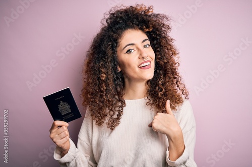 Beautiful tourist woman with curly hair and piercing holding canada canadian passport id with surprise face pointing finger to himself